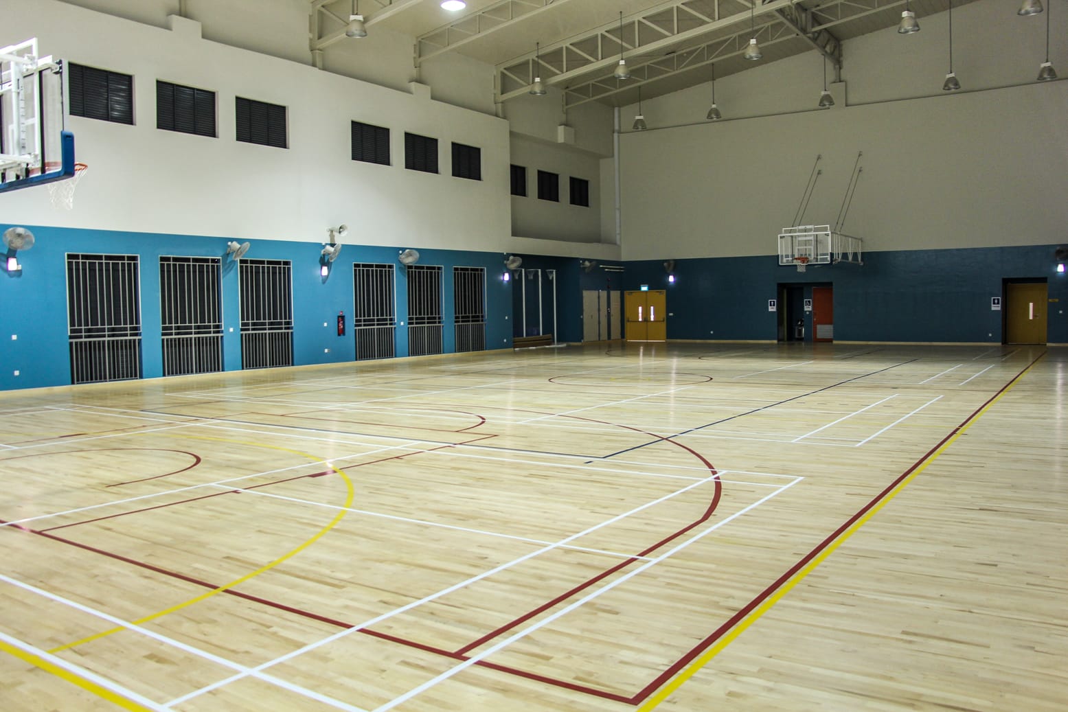 Empty indoor sports hall with a wood floor marked with multicolored court lines and basketball hoops on blue walls.